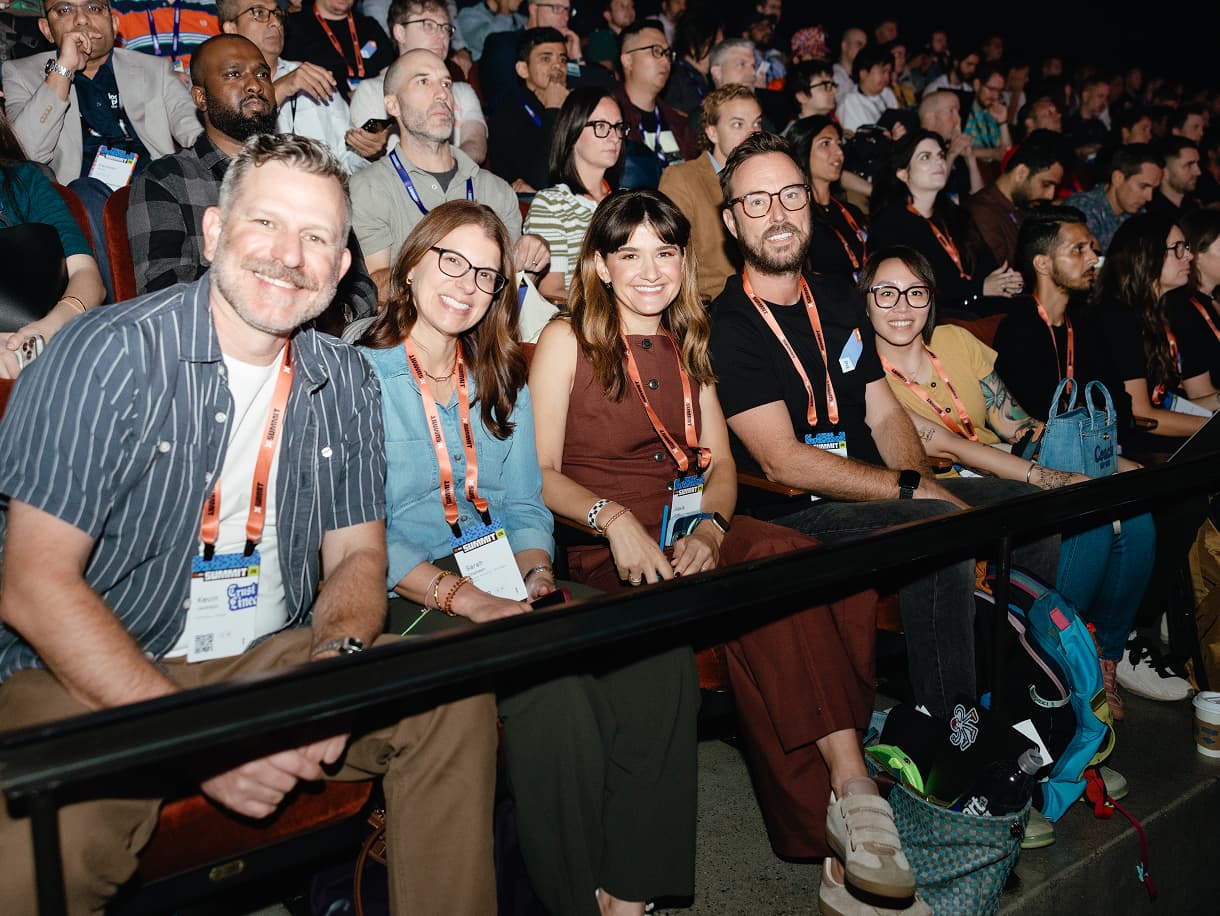 A row of attendees in dbt Summit 2026 lanyards smiling from their keynote seats