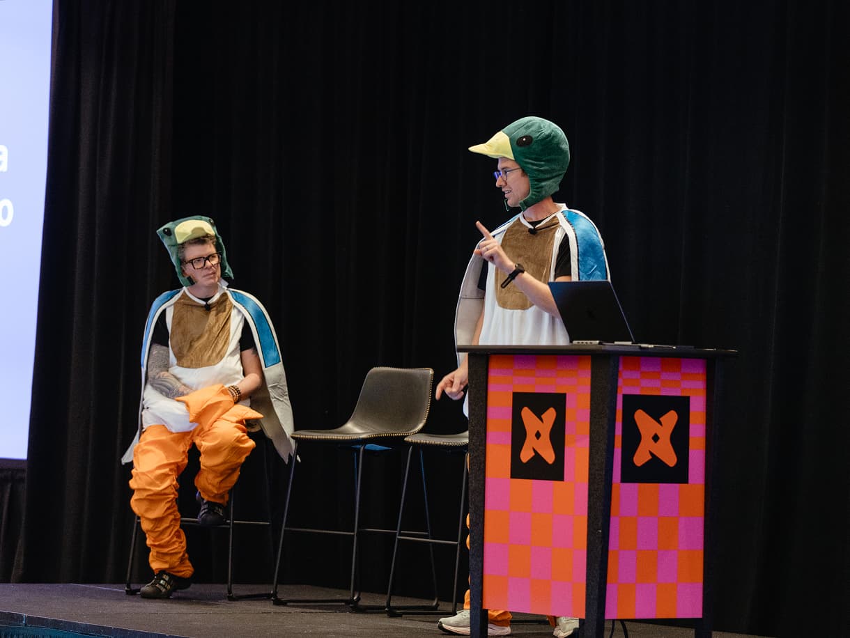 Two speakers in duck costumes presenting from a dbt Summit 2026 podium