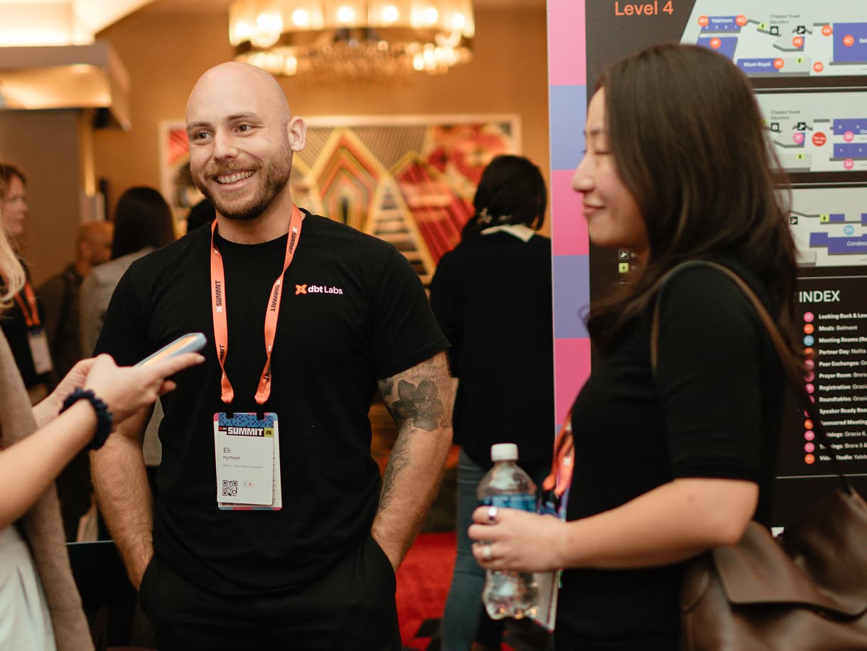 A dbt Labs team member chatting with an attendee beside a dbt Summit 2026 wayfinding sign