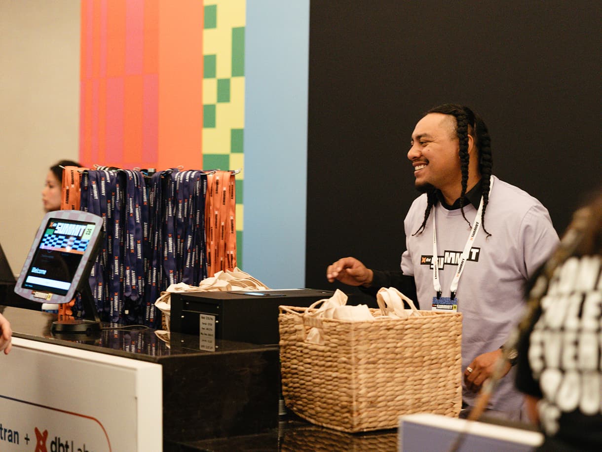 A dbt Summit 2026 staffer handing out tote bags at the merch counter